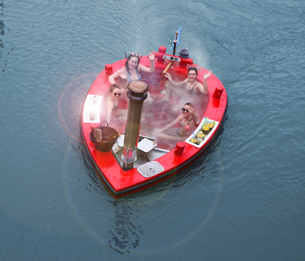Private hot tub boat rental floating in Boston with city skyline and historic ships